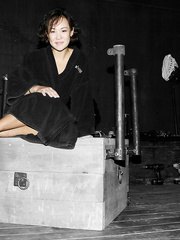 Asian Jandi Lin with playful eyes sits on servitude device wearing dark robe