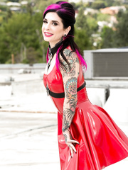 Tattooed female aside a red siren costume to pose naked on a rooftop