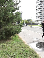 Dark clad Sandra in glasses pauses to pee behind some trees on the street