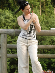 Solo hotty smokes a cigarette up against a rail fence during the time that fully dressed