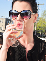 Fully dressed dark brown woman smokes and drinks on patio in sunglasses