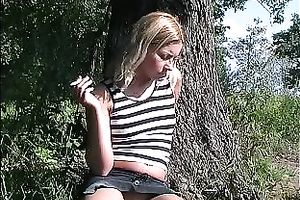 Sweet and hot blondie sitting beneath the tree and flashing her shaved pussy