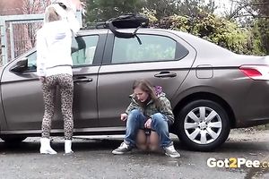 Two European dilettante skanks pissing behind the car