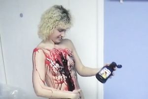 Curly-haired non-professional golden-haired smears her body with paint indoors