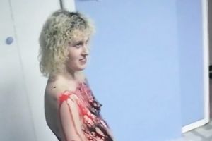 Curly-haired non-professional golden-haired smears her body with paint indoors