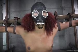 Bounded dark girl with gas mask on her head is crucified